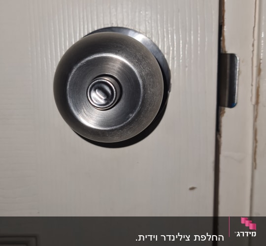ידית דלת מתכתית על דלת עץ לבנה